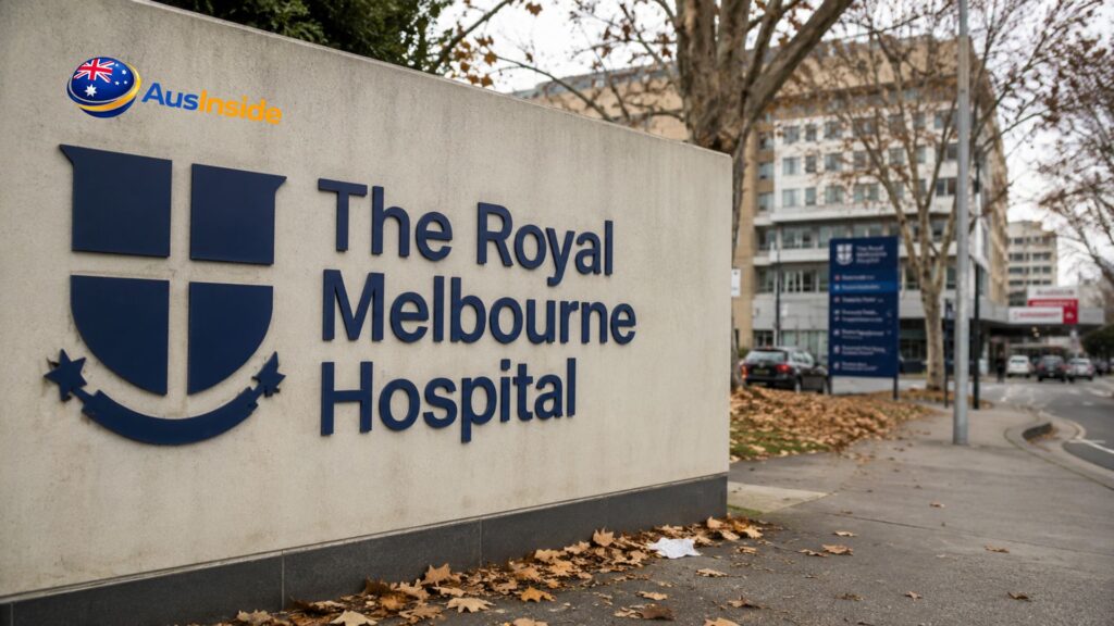Royal Melbourne Hospital entrance sign in Parkville, Victoria, with the hospital building and autumn leaves visible in the background on a cloudy day.