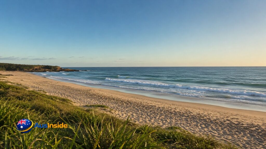 Peaceful view of Pippi Beach in Yamba featuring golden sand, gentle ocean waves, coastal dunes, and a clear blue sky at sunset on the NSW North Coast.
