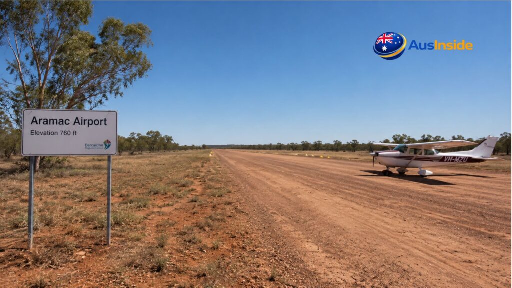 Small aircraft parked beside the gravel runway at Aramac Airport in outback Queensland, with an airport sign and vast rural landscape under a clear blue sky.
