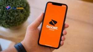 Hand holding a smartphone displaying the Boost Mobile plans app on an orange screen in a modern indoor setting.