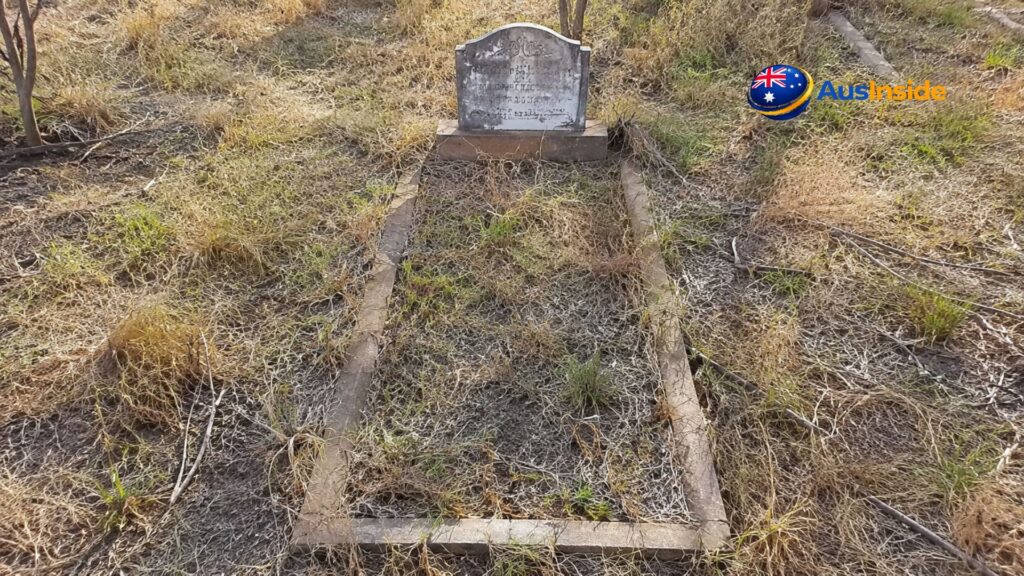 Old weathered grave with a faded headstone surrounded by dry grass and sparse vegetation at Bedourie Cemetery in Queensland's remote outback.