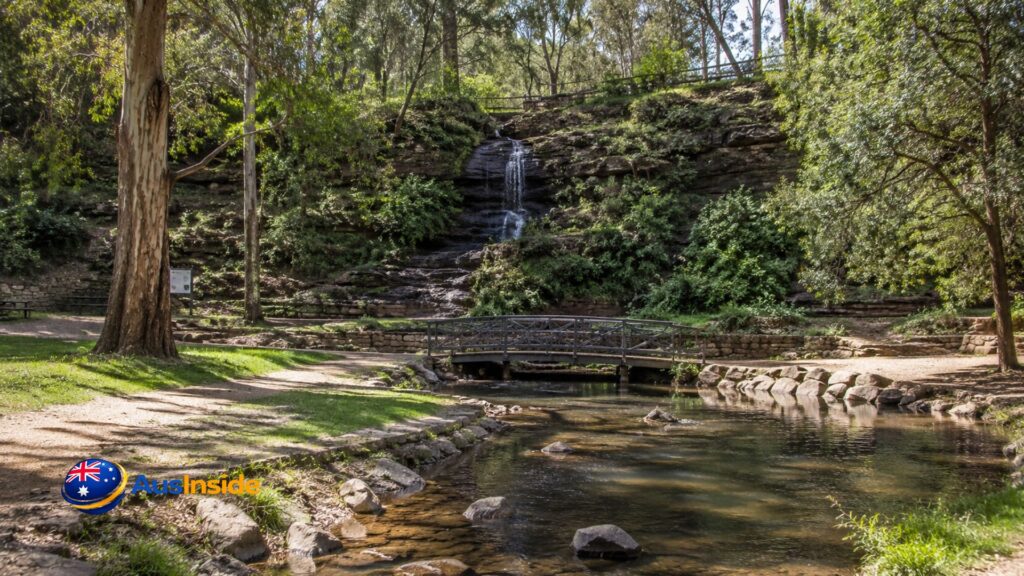 Scenic creek, small wooden bridge, and cascading waterfall surrounded by eucalyptus trees in Belair National Park, South Australia.