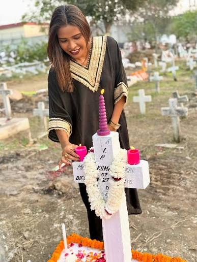 Woman placing a candle and floral tribute on a white cross grave in a cemetery, surrounded by memorial crosses and graves during a remembrance visit.