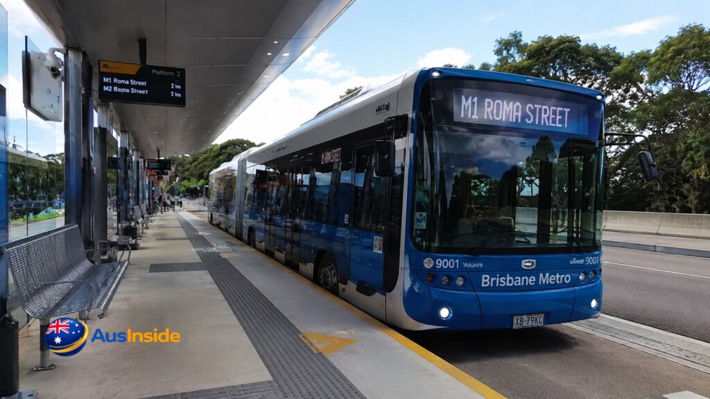 Brisbane Metro M1 bus waiting at a modern station platform with clear destination signage, accessible boarding area, and passengers on a bright day in Brisbane.