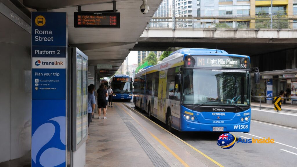 Roma Street Busway Station Platform 1 with an M2 Brisbane Metro bus, Translink signage, landscaped gardens and Brisbane city skyline.