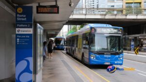Roma Street Busway Station Platform 1 with an M2 Brisbane Metro bus, Translink signage, landscaped gardens and Brisbane city skyline.